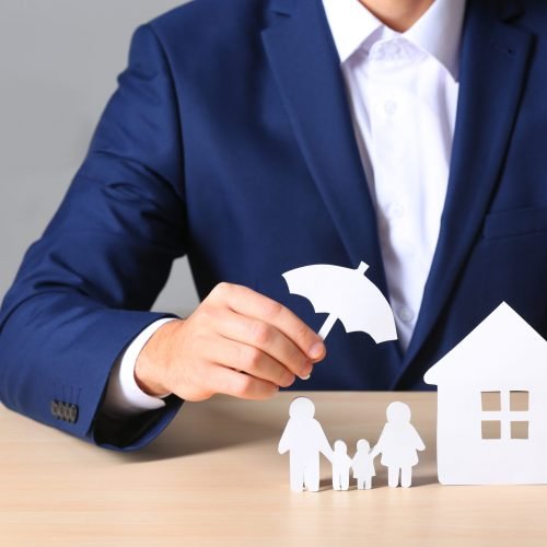 Male insurance agent covering paper family and home with umbrella cutout at table, closeup